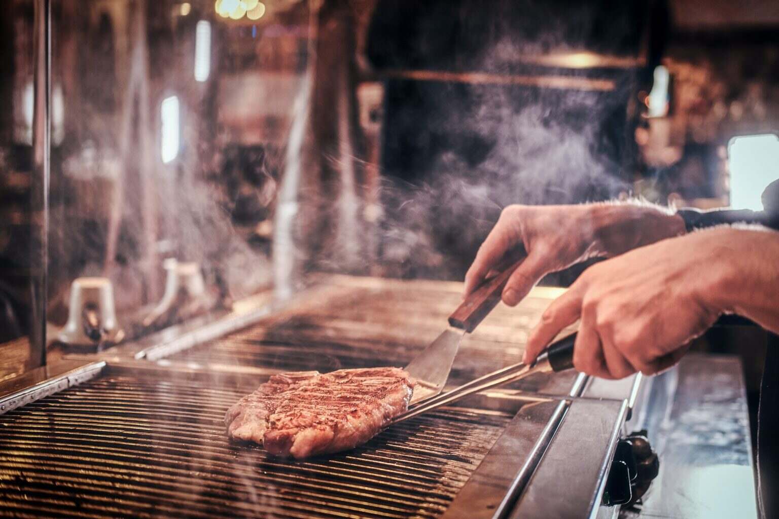 Master chef wearing uniform cooking delicious beef steak on a kitchen in a restaurant