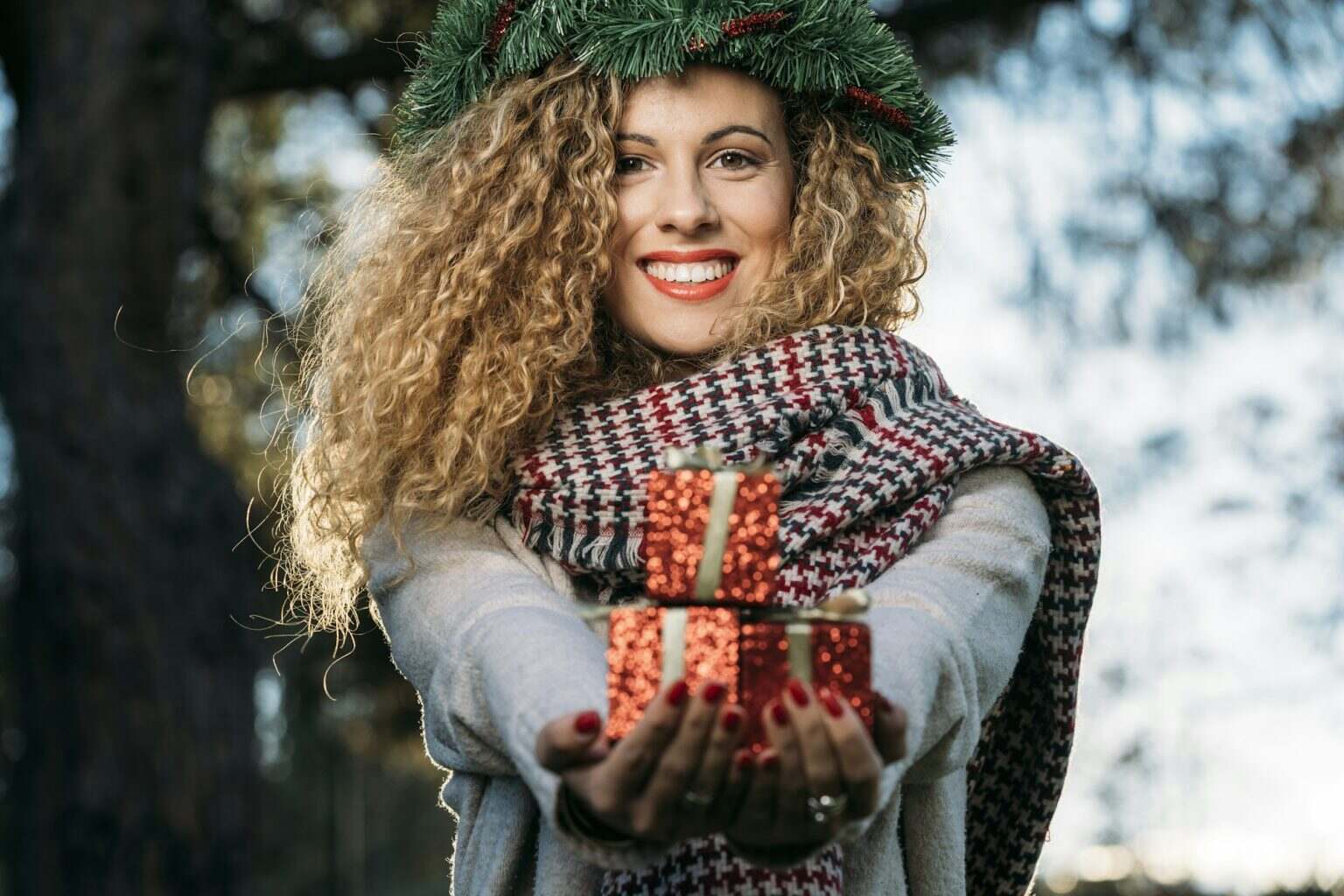 Coiffures pour les fêtes : 5 idées faciles pour tous types de cheveux Portrait of smiling young woman with Christmas wreath on her head presenting Christmas present