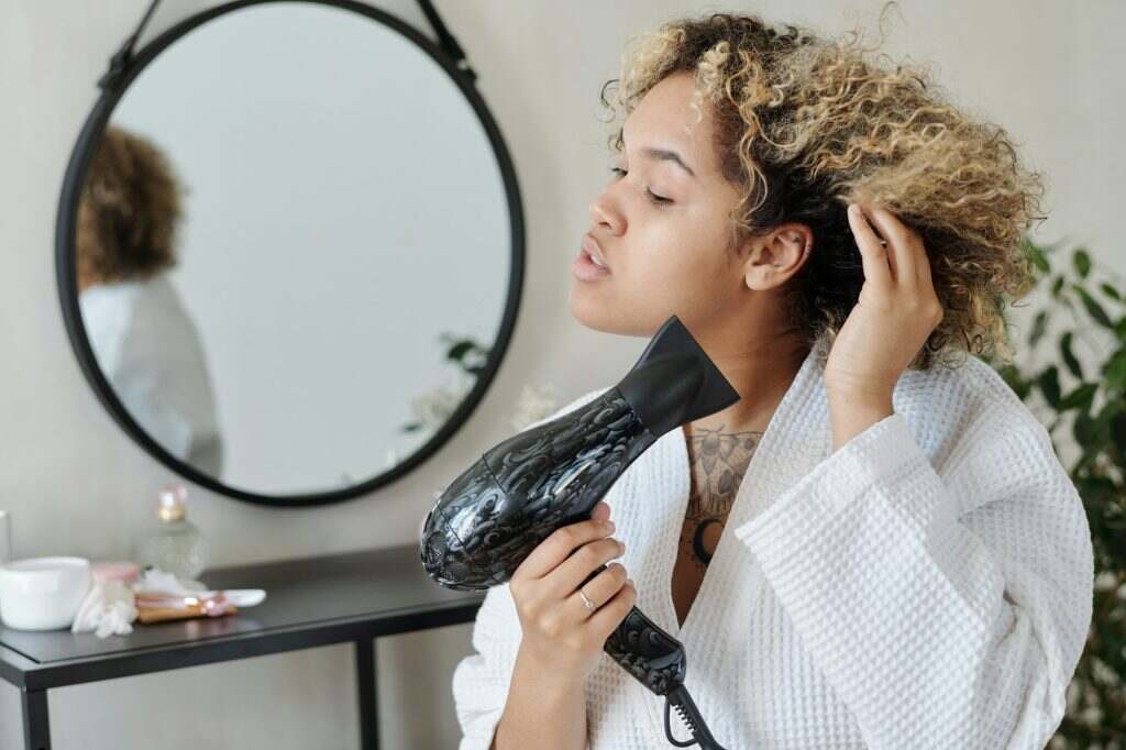 Young black woman using electric hair dryer in front of camera