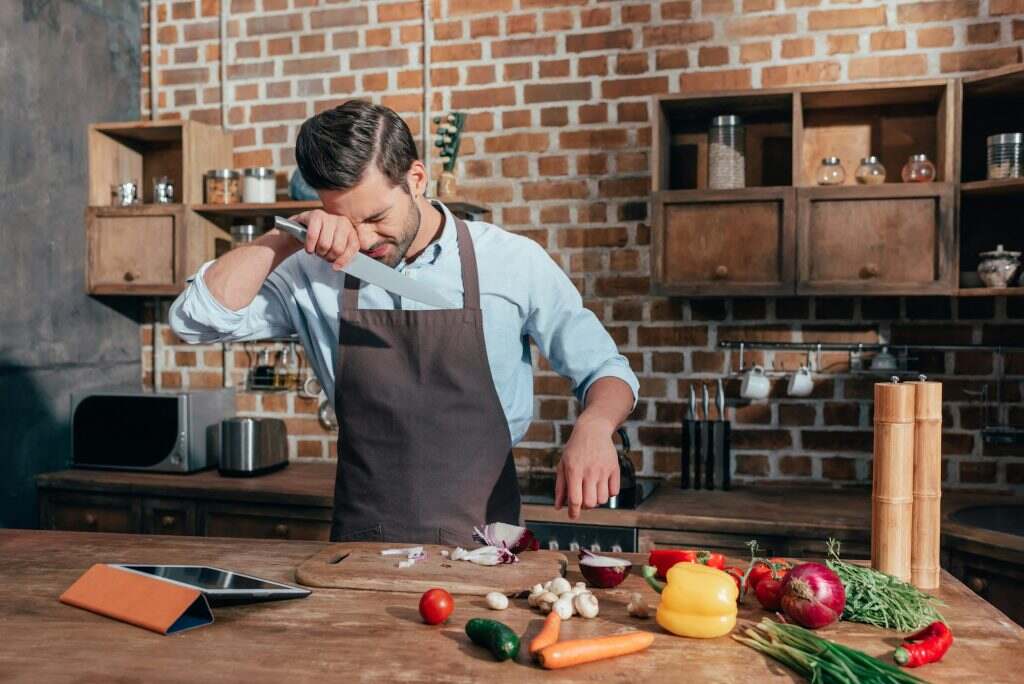 young man crying while cutting onion