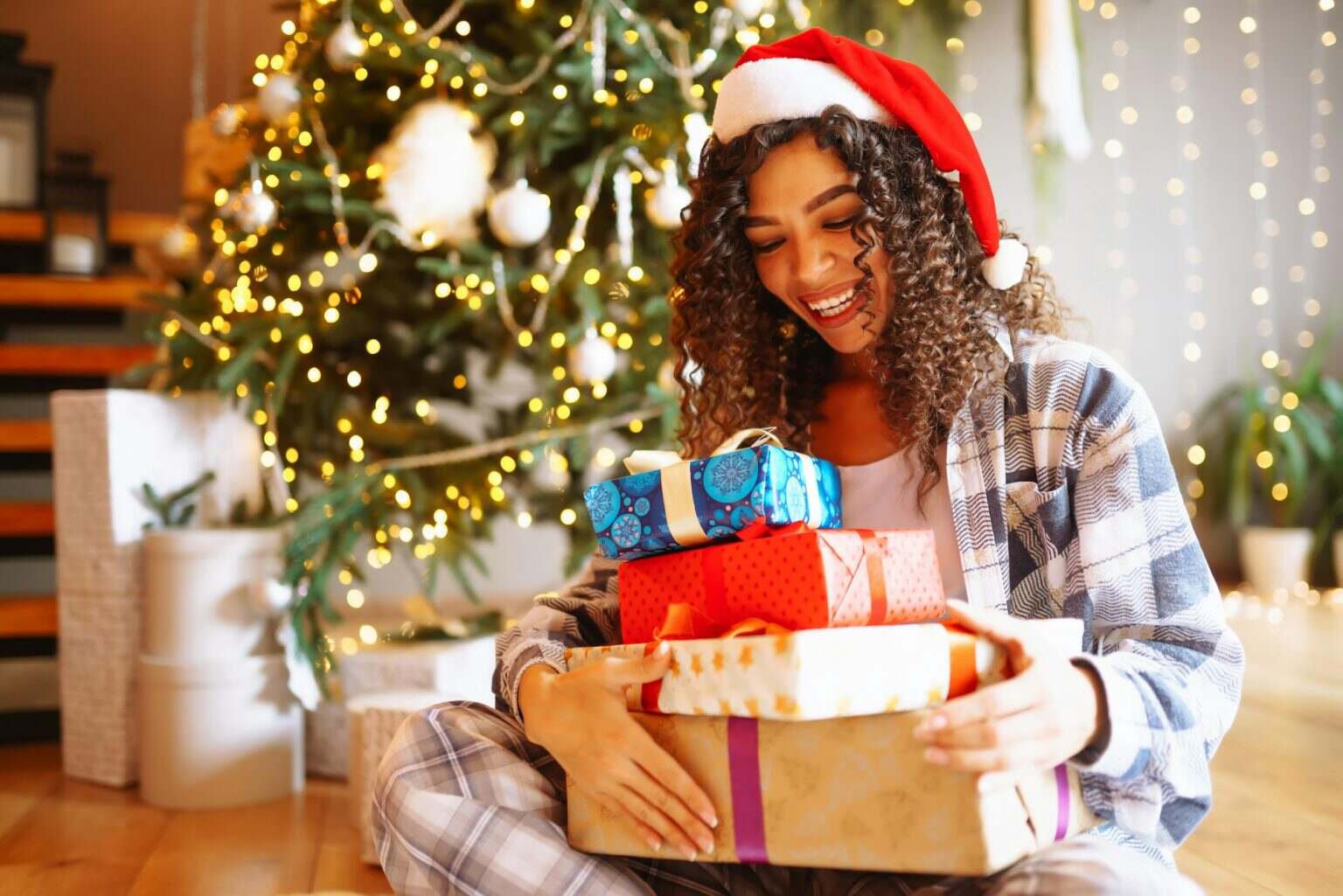 10 villes d’Europe pour vivre un Noël ensoleillé Young woman with Christmas gifts at home near Christmas tree. Winter holidays. New Years.