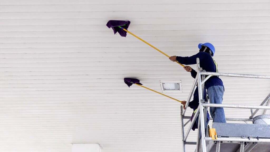 2 workers on scaffolding using flat wet mops to cleaning white ceiling of petrol station