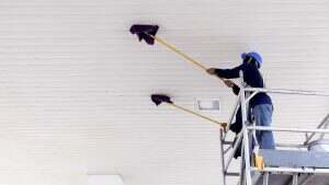 2 workers on scaffolding using flat wet mops to cleaning white ceiling of petrol station