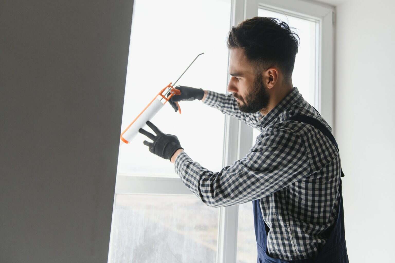 Contractor hand holding glue gun with silicone to repair tile and window.