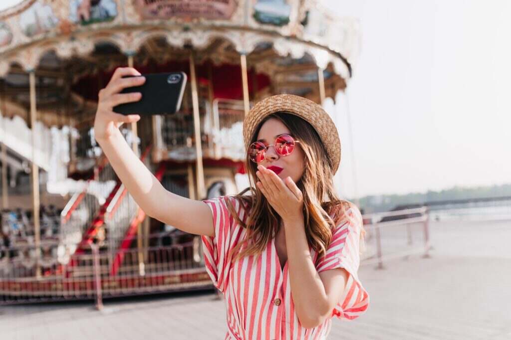 Inspired caucasian girl in straw hat sending air kiss for selfie. Outdoor shot of fascinating woman