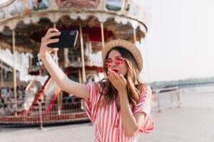 Inspired caucasian girl in straw hat sending air kiss for selfie. Outdoor shot of fascinating woman