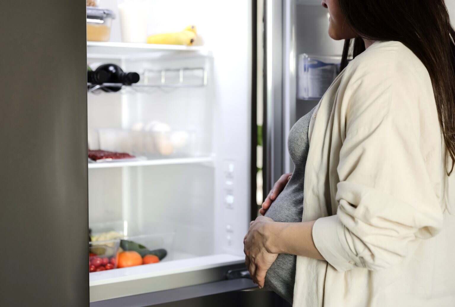 Hungry pregnant woman standing in the front of the opened fridge