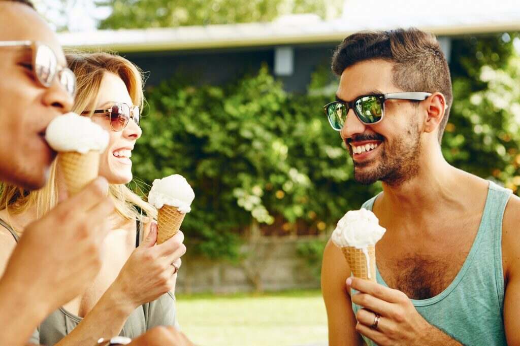 Male and female friends eating ice cream cones in park
