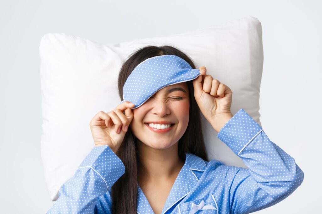 Pleased happy smiling korean girl in blue pajamas and sleeping mask, had great day going bed in