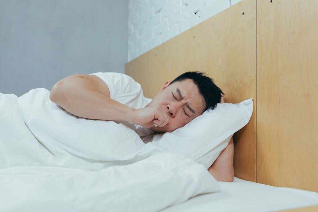 The sick man is lying in bed and coughing, the Asian stayed at home did not go to work depressed