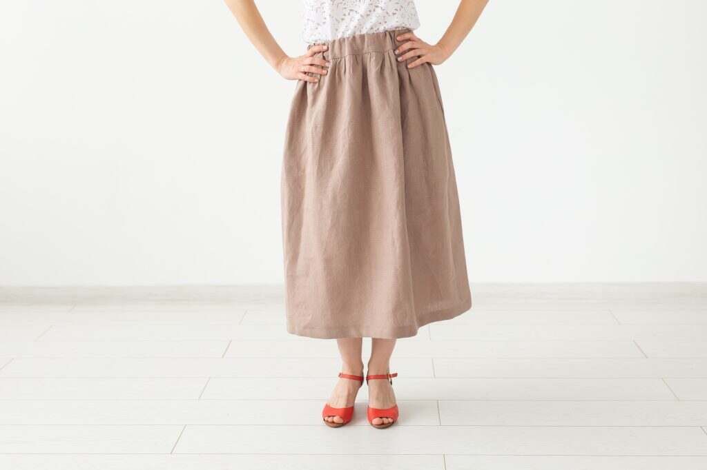 Young unidentified girl in a brown long skirt and shoes stands neara white wall. The concept of