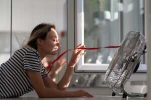 Young woman in striped t-shirt tries to catch airflow from electric fan directing to blonde hair