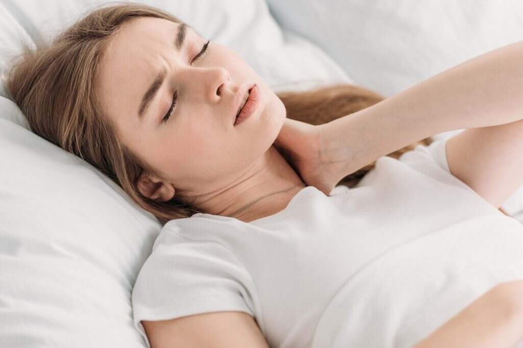young woman lying in bed with closed eyes while suffering from neck pain