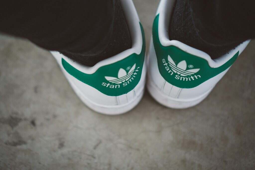 A person wearing green and white adidas sneakers