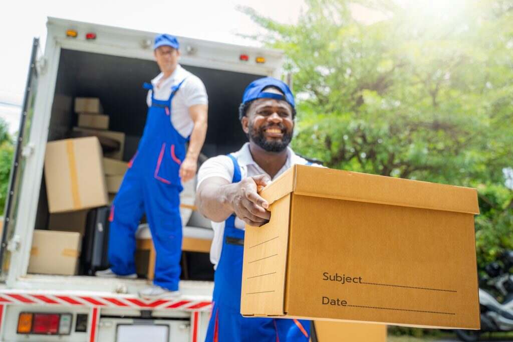 Delivery man unloading moving boxes from car into new home on moving day.