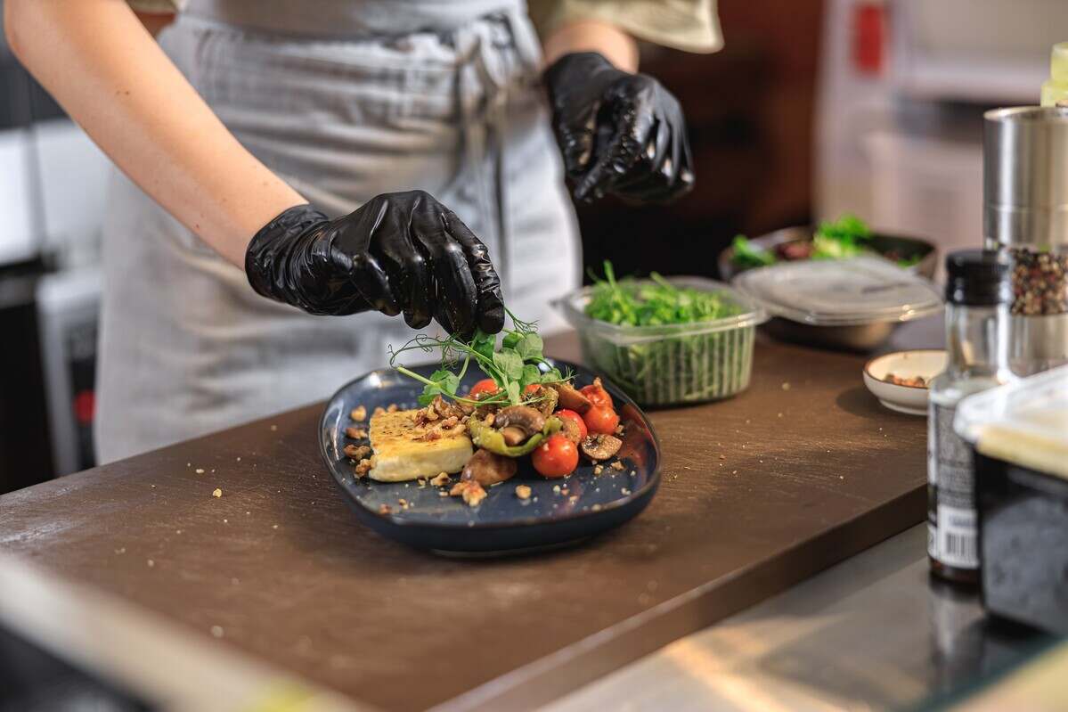 Professional chef is decorating ready meal with greens on restaurant kitchen