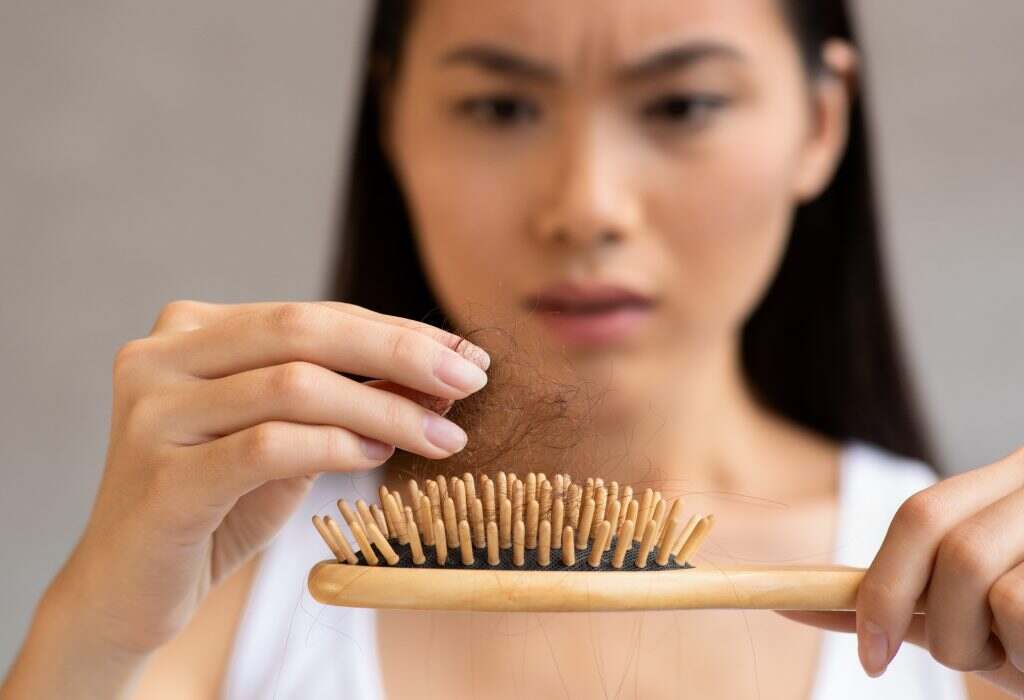 Upset millennial asian woman holding hairbrush, closeup