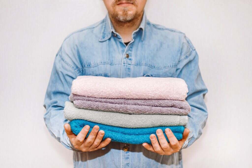 Man holds stack of fresh terry towels. Organization and cleaning of house. Storage and housekeeping