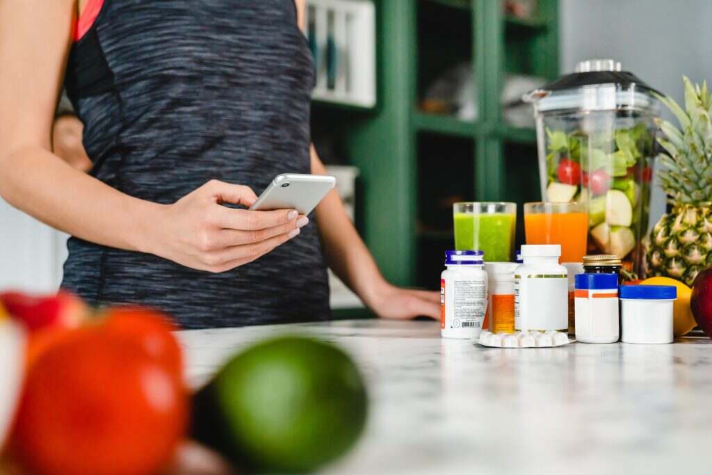 Young woman searching info about food supplements on her phone with fruits and additives