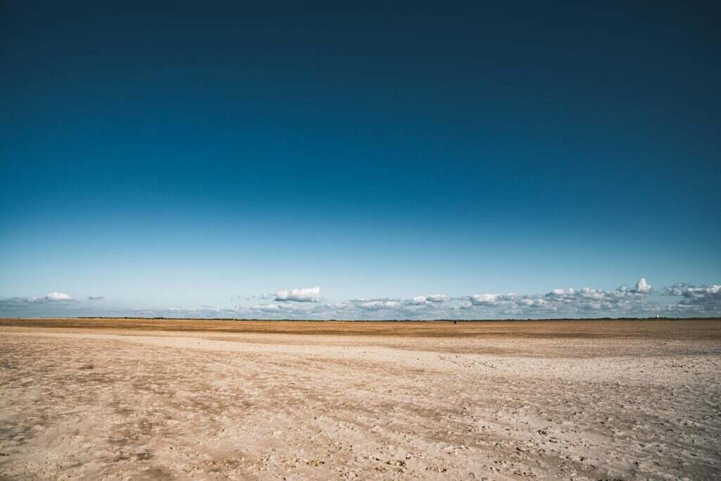 Wide sandy beach with clear blue skies and distant clouds, perfect for nature lovers.