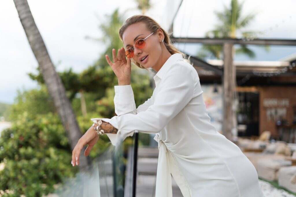 Beautiful young elegant girl in a white dress and orange stylish glasses