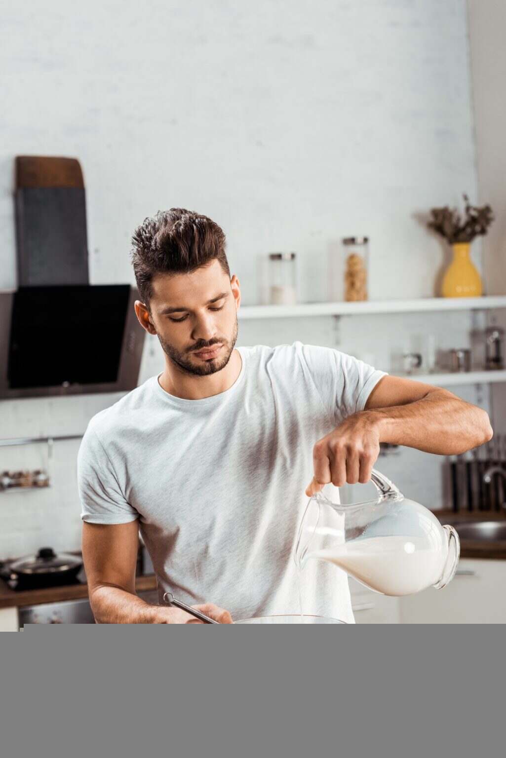 young man pouring milk and cooking omelette at morning