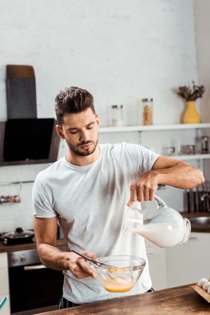 Recette : L’Art de Préparer une Omelette Classique young man pouring milk and cooking omelette at morning