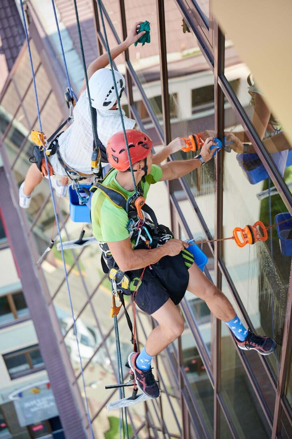 Industrial mountaineering worker cleaning window outside building.