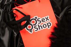 Top view of shopping bag with sex shop lettering near sexual mask on black satin background