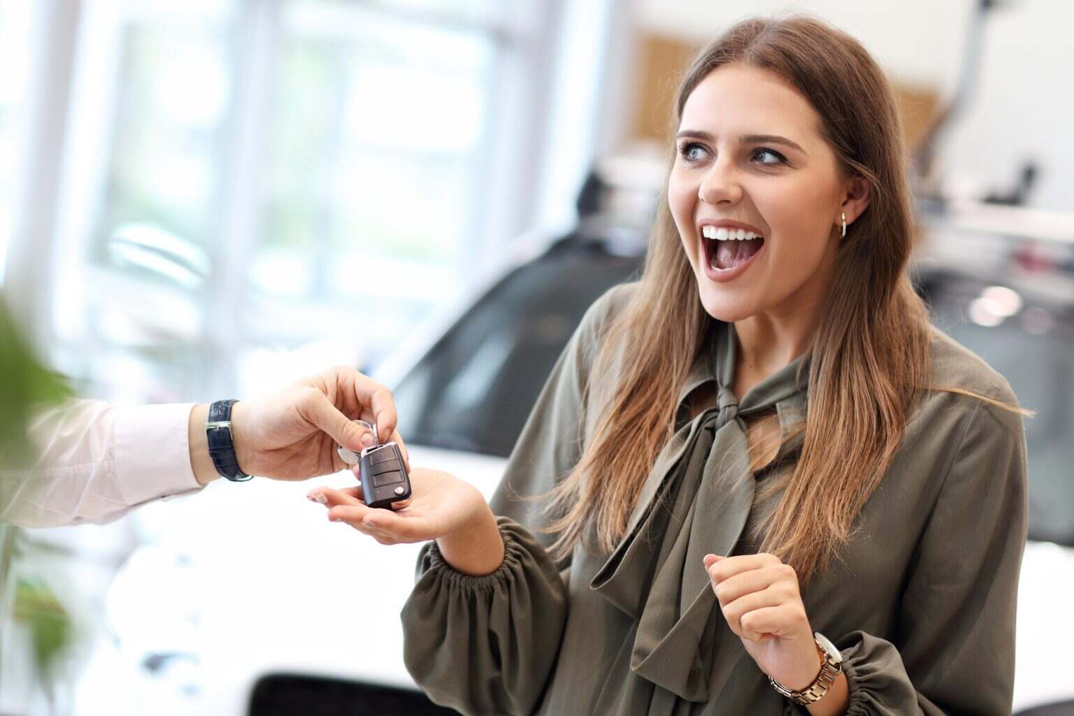 Happy young woman buying car in showroom