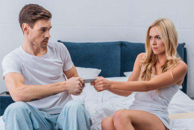 angry young couple fighting for smartphone on bed, mistrust concept