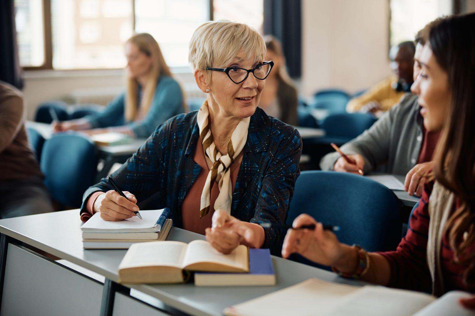 Formation de formateur pour adultes : révélez le pédagogue qui sommeille en vous Female adult learners communicating during a class in lecture hall.