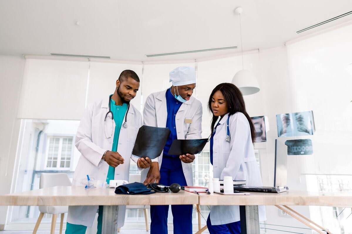 Healthcare, medical: Group of three young African doctors, two men and woman, discuss and looking x