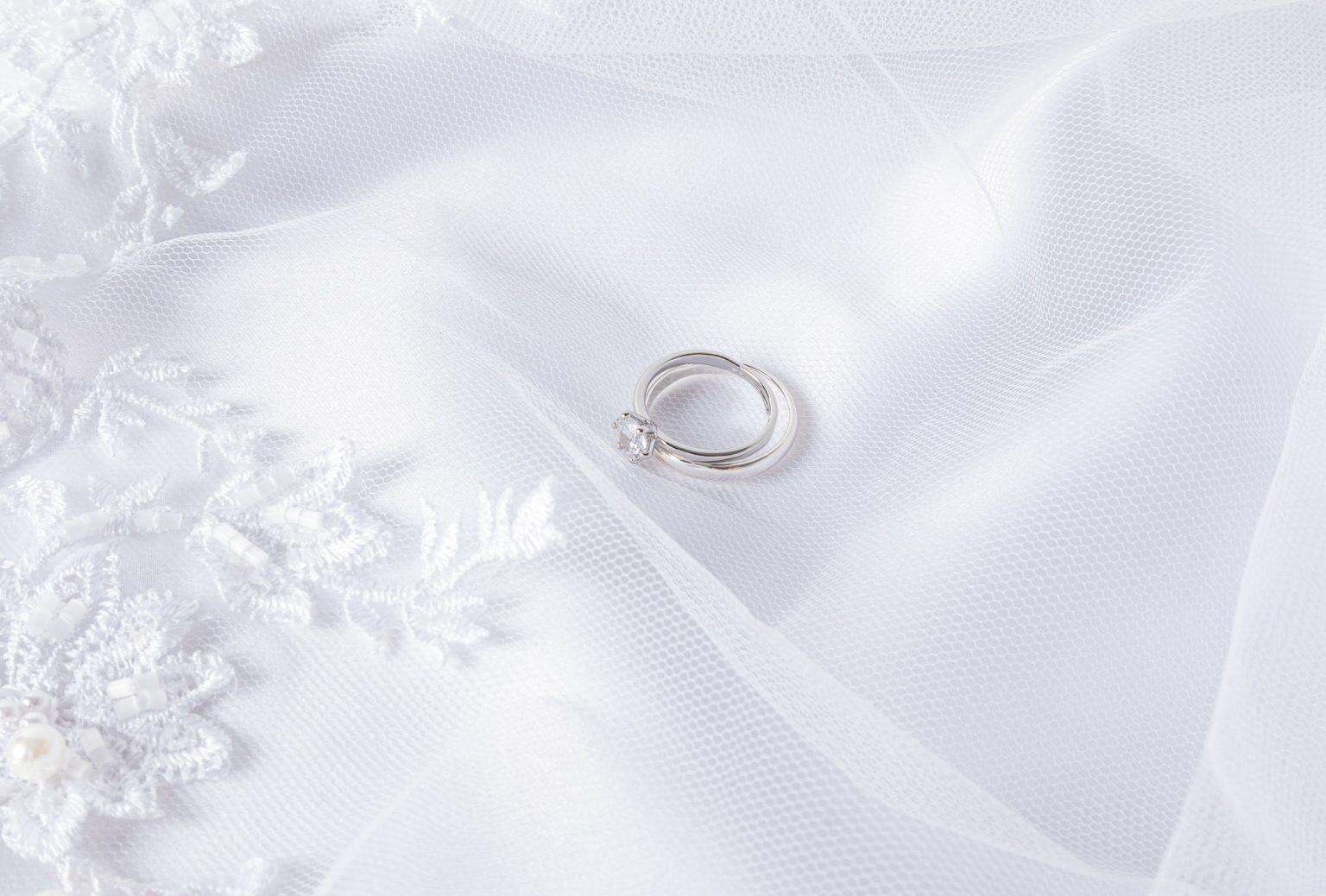 Broderie diamant : quand les strass deviennent thérapie et art Two wedding rings made of white gold with a diamond lie on a white veil with soft pleats. Wedding
