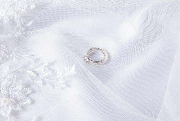 Two wedding rings made of white gold with a diamond lie on a white veil with soft pleats. Wedding