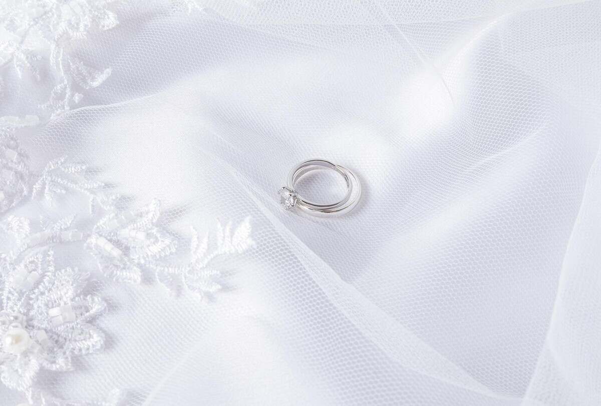 Two wedding rings made of white gold with a diamond lie on a white veil with soft pleats. Wedding