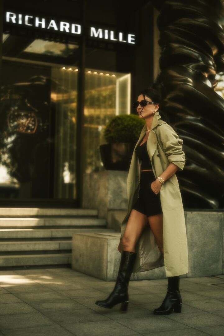Fashionable woman in trench coat and knee-high boots walking past Richard Mille store.