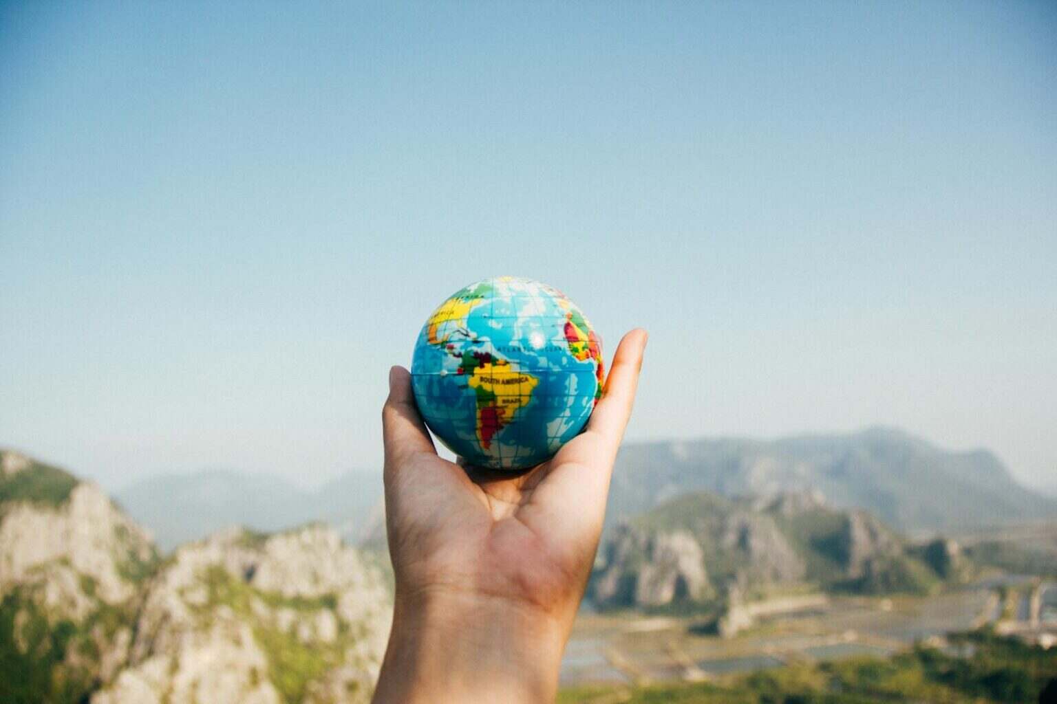 L’assurance voyage longue durée : un indispensable pour votre tranquillité d’esprit Hand holding a globe against a mountain background symbolizing travel and exploration.