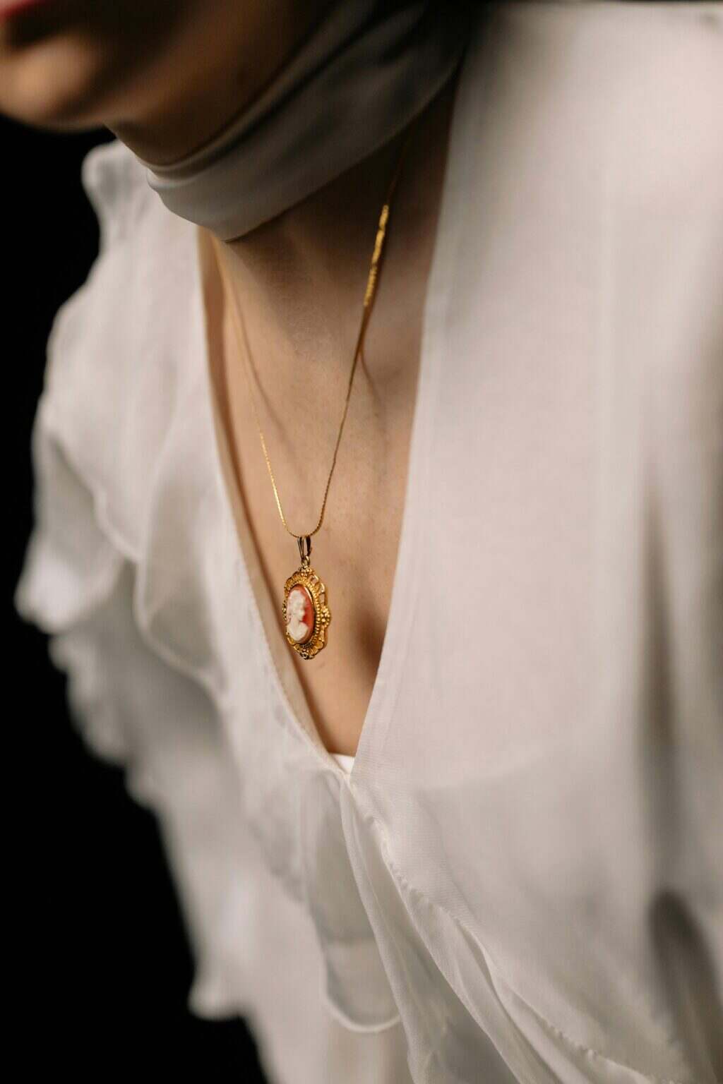 Close-up of a woman wearing a gold cameo necklace and white blouse, conveying elegance and sophistication.