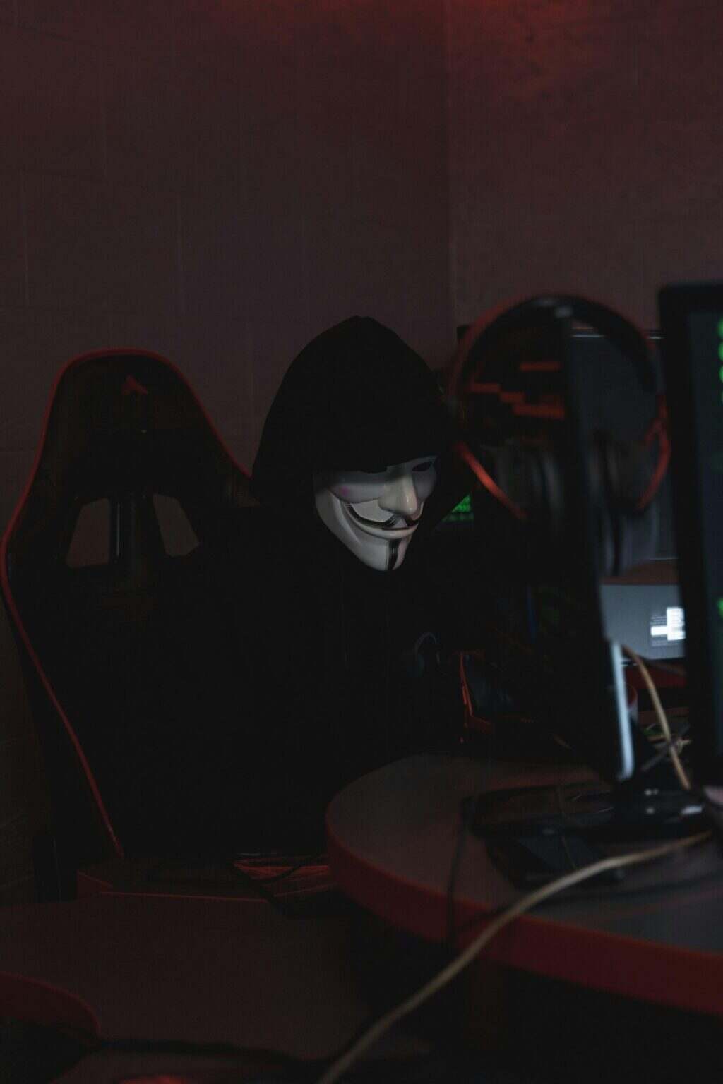 A hacker in a Guy Fawkes mask working on cybersecurity at night, conveying secrecy.