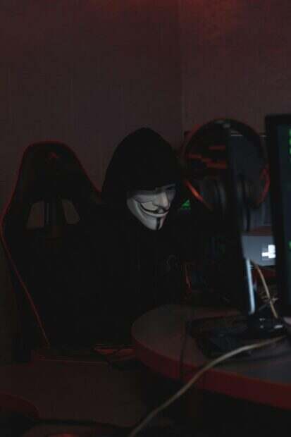 A hacker in a Guy Fawkes mask working on cybersecurity at night, conveying secrecy.