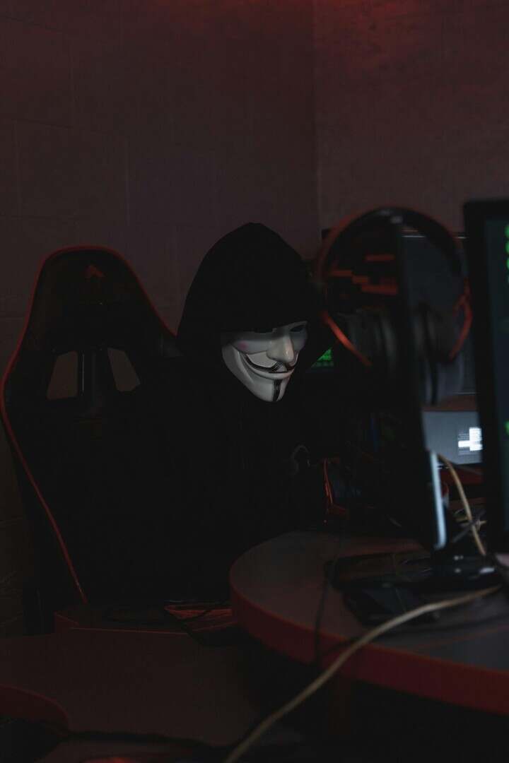 A hacker in a Guy Fawkes mask working on cybersecurity at night, conveying secrecy.