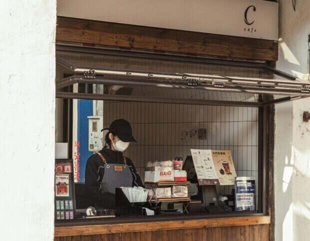A worker behind the counter of an outdoor cafe kiosk, preparing orders.