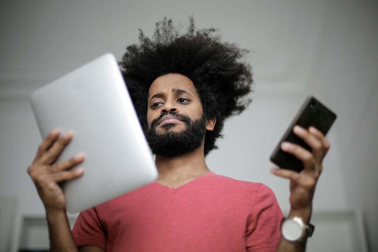 Man indoors comparing a smartphone and tablet with a thoughtful expression, highlighting technology engagement.