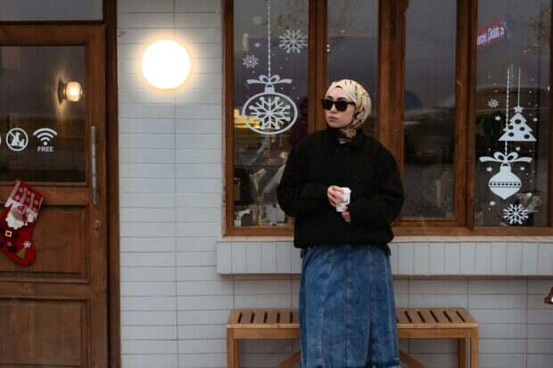 A stylish woman enjoys coffee outside a cafe with winter decorations.