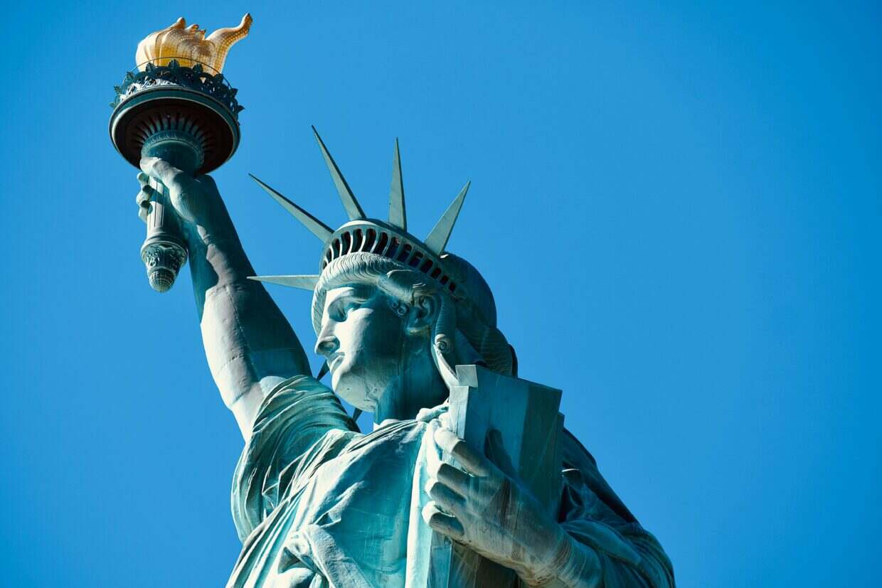 Close-up of the Statue of Liberty's torch and face against a clear blue sky in New York.