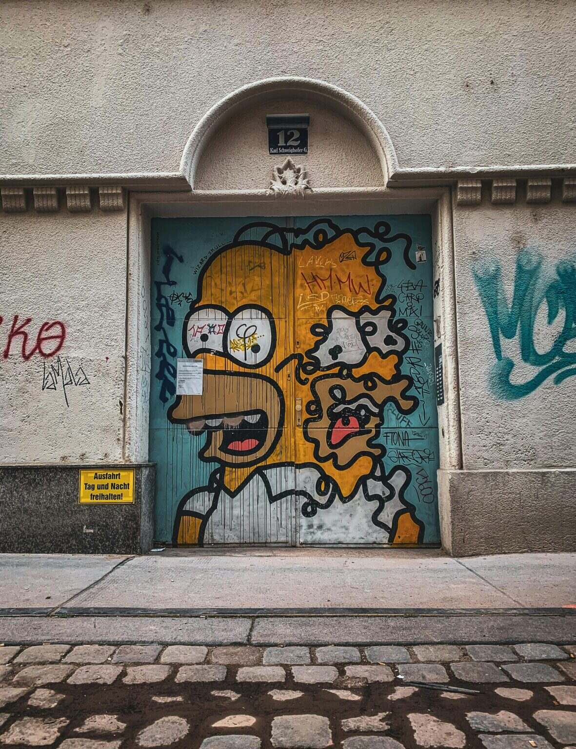 Les Simpson Saison 36 : Une Rencontre Historique entre Deux Homers Street art of a popular cartoon character on a Viennese building door, showcasing urban creativity.