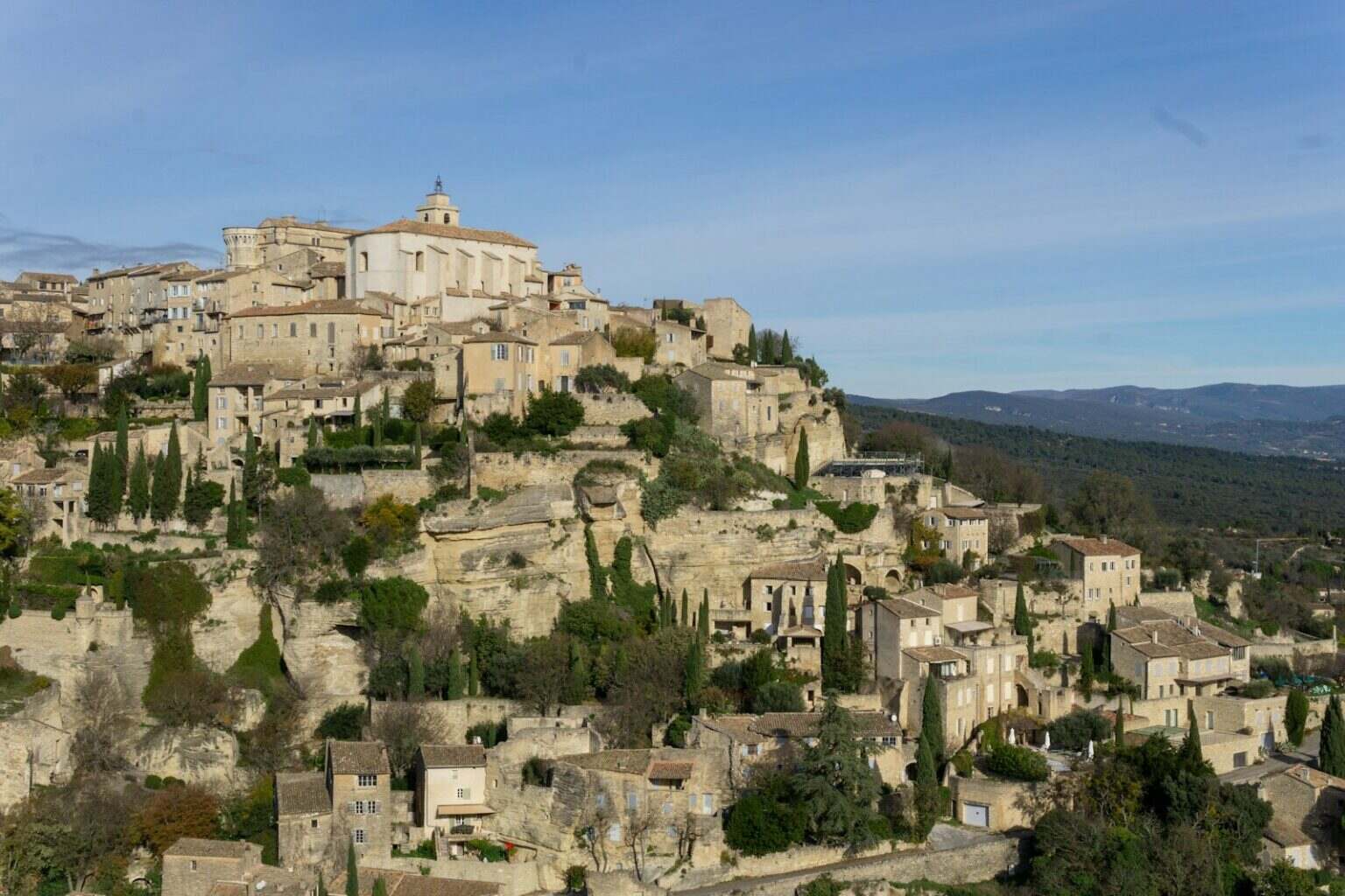 Partir en vacances en Provence : une bonne idée pour juillet-août ? Hilltop village with ancient stone buildings and cypress trees.