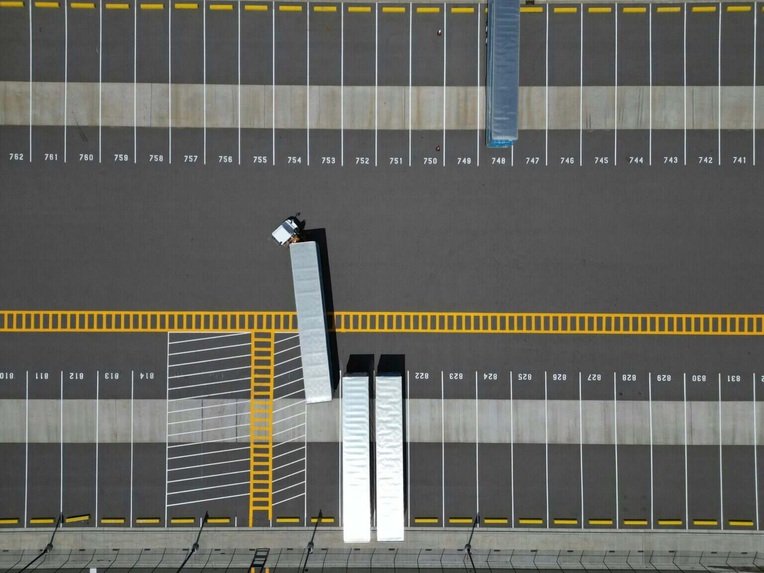 An aerial view of a large parking lot with lined spaces and semi-trucks.