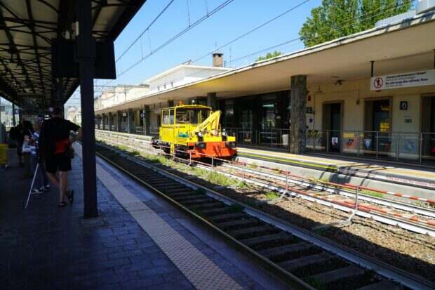 Photograph of a yellow maintenance vehicle on tracks with people waiting on the platform.